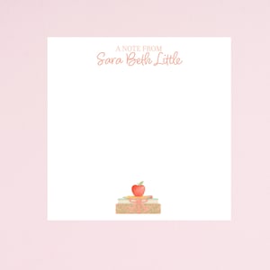 May include: White notepad with the text "A Note From Sara Beth Little" in a peach color. A stack of books, pencils, and a red apple with a green leaf are at the bottom. A pink ribbon is tied around the books.