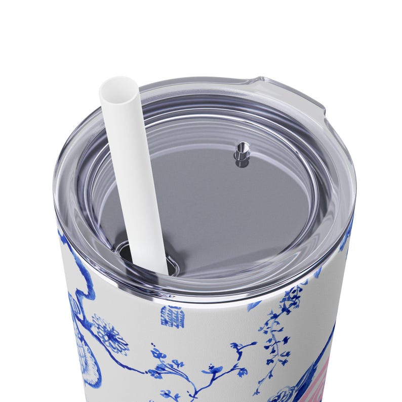 May include: A white stainless steel tumbler with a blue and white floral design. The tumbler has a clear lid with a hole for a straw. A white straw is inserted through the hole in the lid.