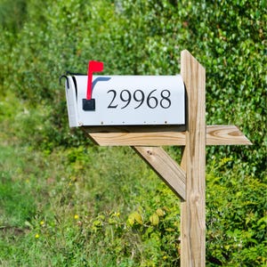 May include: A white mailbox with the number "29968" in black. The mailbox has a red flag and is mounted on a wooden post. The background is filled with green foliage.