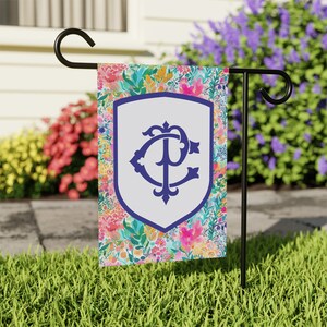 Peut inclure: Un drapeau de jardin avec un bouclier blanc orn&eacute; d'un monogramme bleu "PC" entour&eacute; d'un motif floral color&eacute;.
