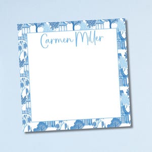 May include: A square notepad with a white interior and a blue and white Chinoiserie-style border. The name "Carmen Miller" is written in light blue script across the top of the notepad.