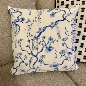 May include: A white throw pillow with a blue floral pattern featuring branches, flowers, and pagodas. The pillow is on a gray couch.