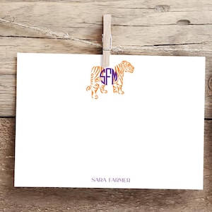 May include: A white card with an orange tiger silhouette with a purple monogram "SFM" in the center. The text "SARA FARMER" is printed at the bottom of the card.