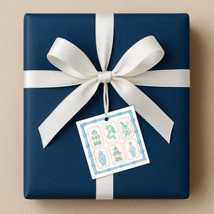May include: A wrapped gift with navy blue paper and a white satin ribbon tied in a bow. A gift tag with six decorative illustrations in blue, pink, and green is attached to the bow.