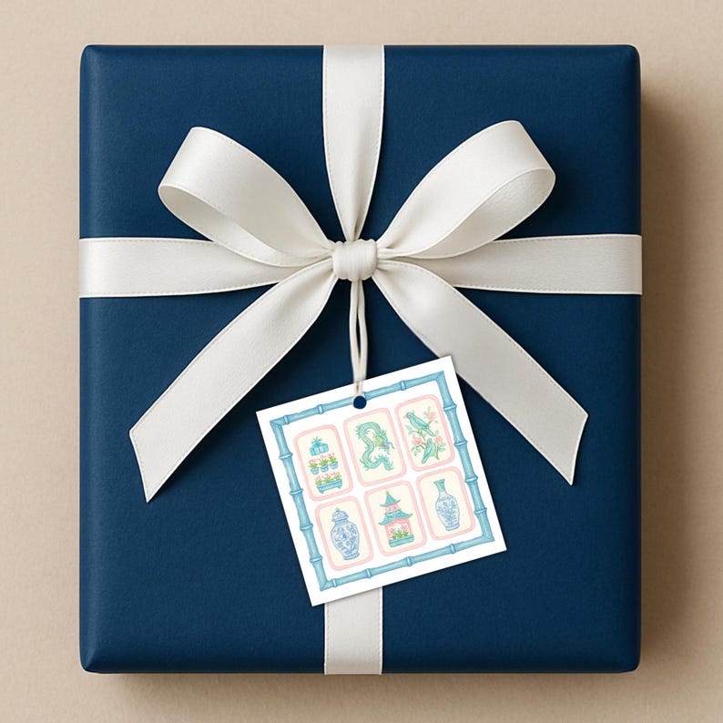 May include: A wrapped gift with navy blue paper and a white satin ribbon tied in a bow. A gift tag with six decorative illustrations in blue, pink, and green is attached to the bow.