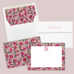 May include: Stationery set featuring a floral pattern in pink and green on a light pink background. The set includes envelopes, a card, and a notecard with a monogram. The address is printed on the envelope.