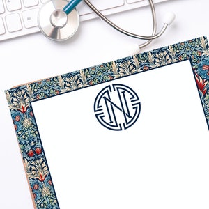 May include: A white sheet of paper with a blue and red floral border. The letter "N" is in a circle in the center of the paper.