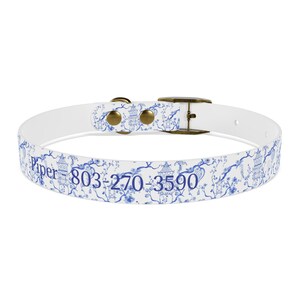 Op de afbeelding: Witte hondenband met een blauw en wit bloemenpatroon en de tekst "Piper 803-270-3590".