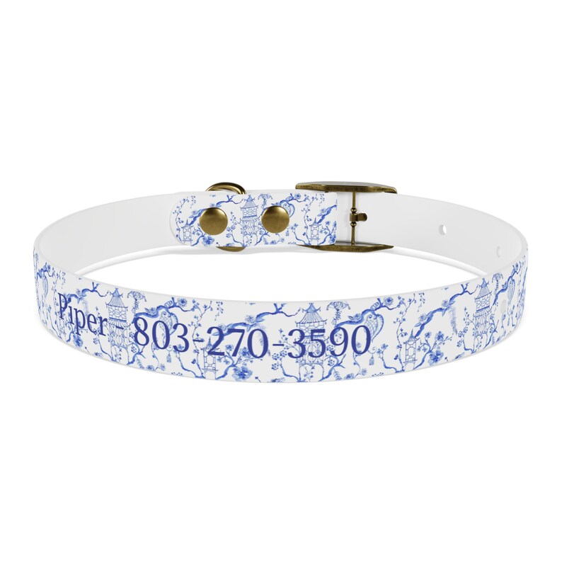 Op de afbeelding: Witte hondenband met een blauw en wit bloemenpatroon en de tekst "Piper 803-270-3590".