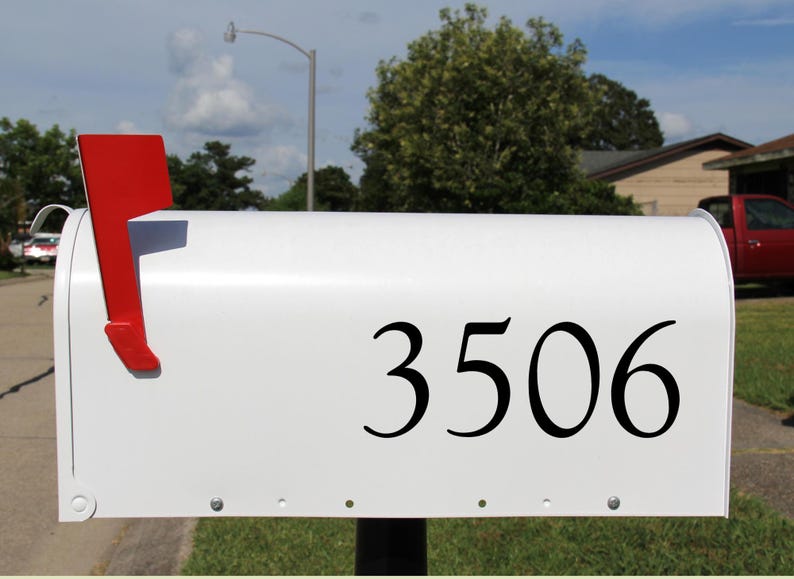 May include: A white mailbox with the number 3506 in black. The mailbox has a red flag on the side, indicating mail delivery. The scene is outdoors on a sunny day.