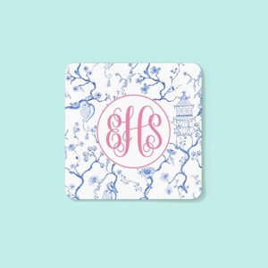 May include: Square coaster with a white background featuring a blue floral pattern and a pink monogram. The monogram is in a pink circle and features the letters EHS.