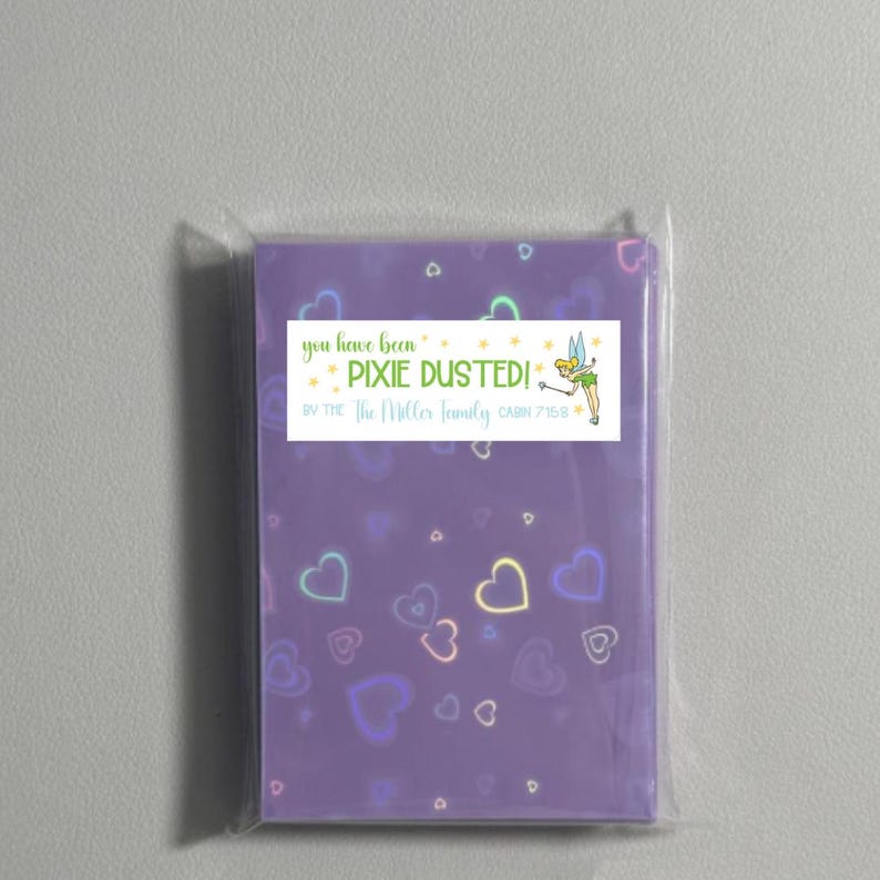 May include: A purple card with a heart pattern and a sticker that says "You have been Pixie Dusted! By the Miller family Cabin 7158" with a cartoon image of Tinkerbell.