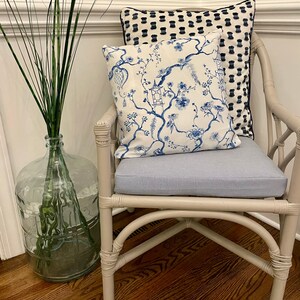 May include: A white wicker chair with a blue and white floral patterned pillow and a black and white patterned pillow. The chair is sitting on a wooden floor.