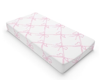 May include: A white fitted crib sheet with a pink bow pattern.
