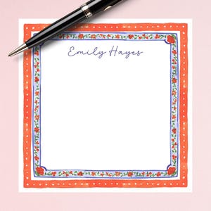 May include: A white notepad with a red and blue floral border. The name "Emily Hayes" is written in blue ink at the top of the notepad.