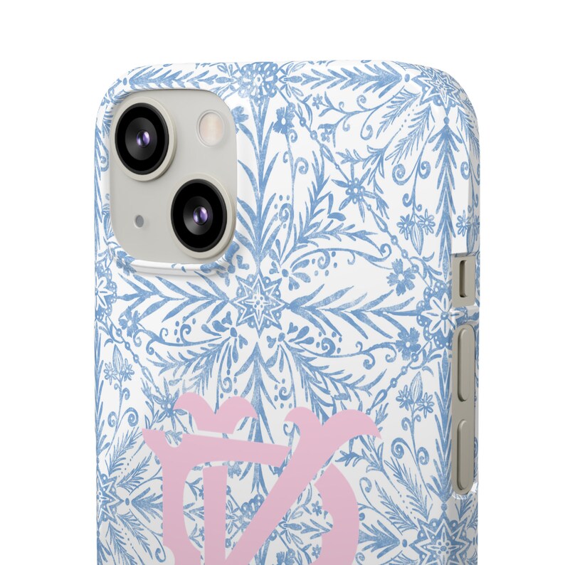 May include: A white phone case with a blue and white floral pattern. The case has a pink monogram in the centre.