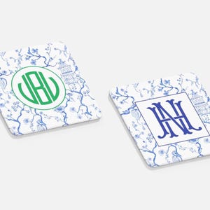 May include: Two square coasters with a white background and a blue floral pattern. One coaster has a green monogram, the other has a blue monogram. Both have a pagoda design.