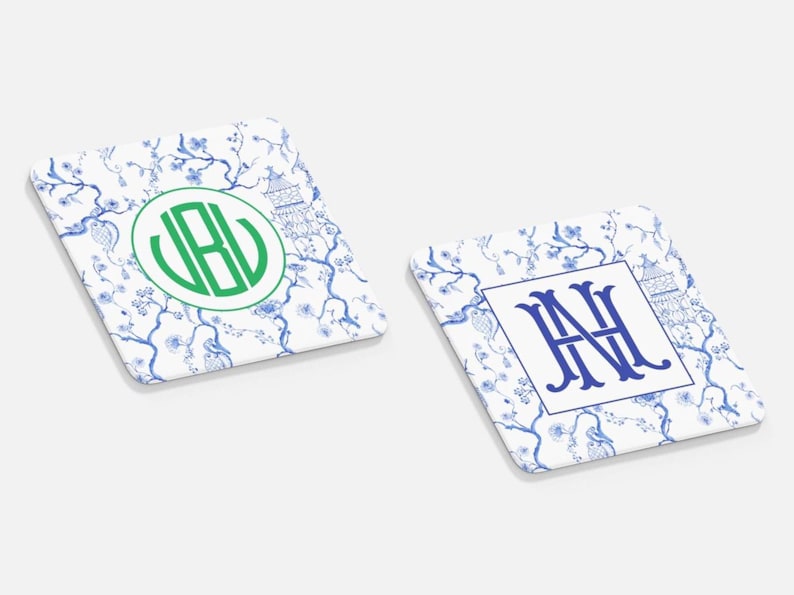May include: Two square coasters with a white background and a blue floral pattern. One coaster has a green monogram, the other has a blue monogram. Both have a pagoda design.