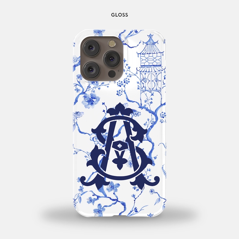 May include: A white phone case with a blue and white floral design. The design features a pagoda, a monogram, and a floral pattern. The case is glossy.