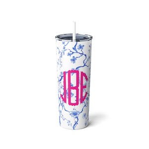 May include: A white stainless steel tumbler with a blue and white floral pattern and a pink monogram "JBE".