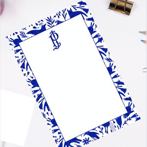 Peut inclure: Bloc-notes blanc avec une bordure bleue ornée d'un motif floral et d'oiseaux stylisés. Le bloc-notes porte un monogramme bleu "P" dans le coin supérieur gauche.