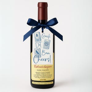 May include: A bottle of Cabernet Sauvignon wine with a dark red bottle top and a navy blue ribbon tied around the neck. A tag with the words "Crack Dot Bam Cheers!" is attached to the ribbon. The label reads "Napa Valley".
