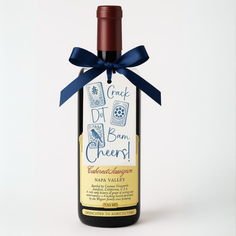 May include: A bottle of Cabernet Sauvignon wine with a dark red bottle top and a navy blue ribbon tied around the neck. A tag with the words "Crack Dot Bam Cheers!" is attached to the ribbon. The label reads "Napa Valley".