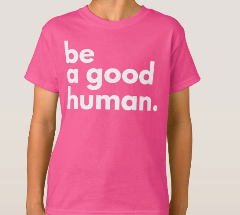 May include: Pink t-shirt with white text that reads "be a good human."