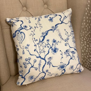 May include: A white throw pillow with a blue and white floral pattern. The pattern features branches with blue flowers, leaves, and a birdcage.