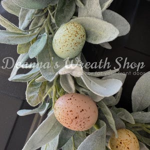 May include: A wreath made of faux lambs ear greenery with speckled Easter eggs in shades of brown, yellow, and blue.