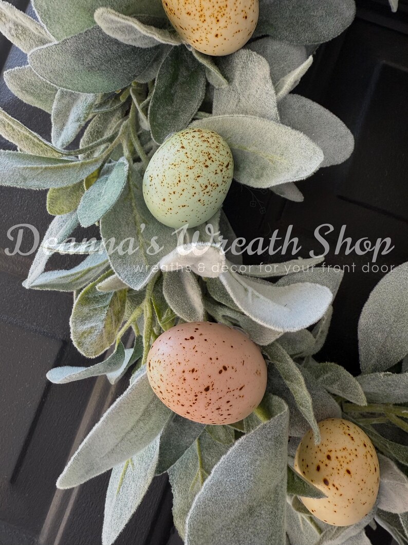 May include: A wreath made of faux lambs ear greenery with speckled Easter eggs in shades of brown, yellow, and blue.