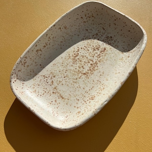 Op de afbeelding: Een rechthoekige serveerschaal van wit keramiek met een gespikkeld bruin glazuur.