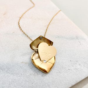 Puede incluir: Un collar con un colgante en forma de corazón dorado. El relicario se abre para revelar un corazón más pequeño con el texto grabado "I love my family!". El collar tiene una cadena delicada.