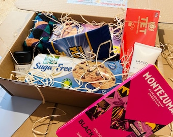 May include: A gift box filled with various items, including a box of cookies, a bag of peanuts, a tube of lotion, a jar of spices, a box of tea, and a bar of chocolate. The box is lined with paper and contains a pair of patterned socks.