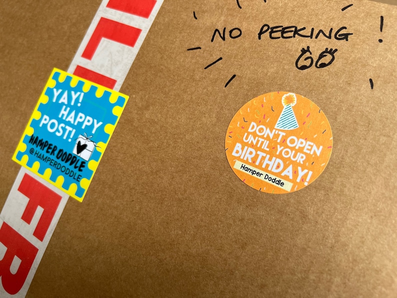 May include: A brown cardboard box with a yellow and blue sticker that says "YAY! HAPPY POST!" and a yellow sticker with confetti and the text "DON'T OPEN UNTIL YOUR BIRTHDAY!"  The box also has a red and white label that says "LIF" and handwritten text that says "NO PEEKING!"