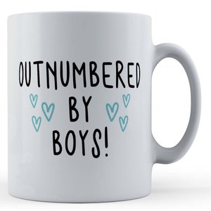 May include: White ceramic mug with black text that reads "Outnumbered by Boys!" with blue hearts around the text.