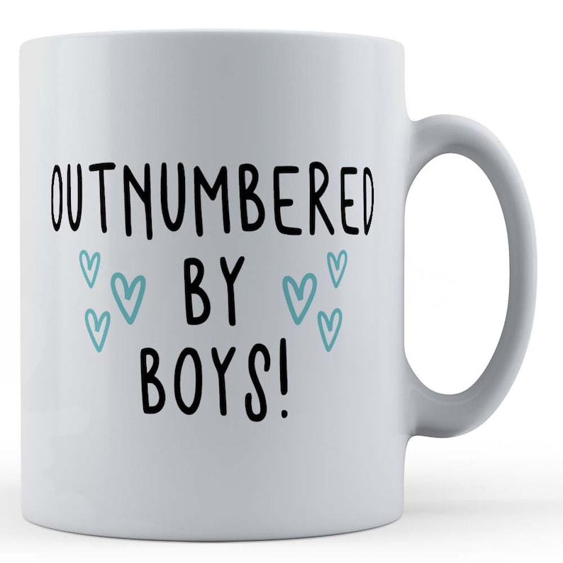 May include: White ceramic mug with black text that reads "Outnumbered by Boys!" with blue hearts around the text.