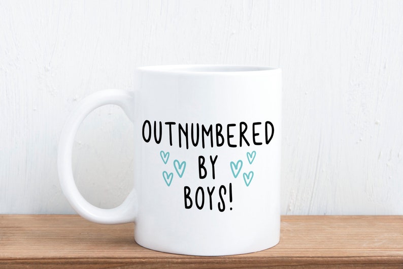 May include: White ceramic coffee mug with black text that reads "Outnumbered by Boys!" with blue heart illustrations.