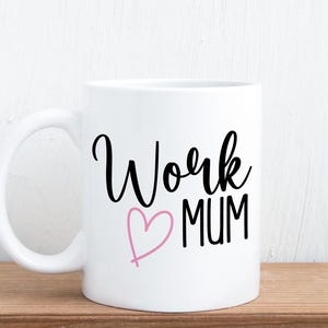 May include: A white ceramic mug featuring the black text Work and MUM in a stylised font, with a pink hand-drawn heart outline positioned between the two words. The mug has a standard handle and a smooth, glossy finish on its exterior surface.