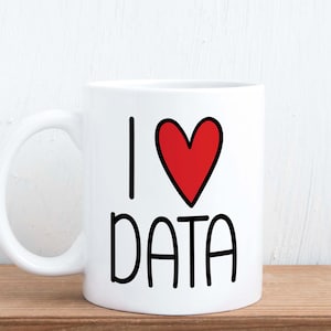 May include: White ceramic mug with the text "I ❤️ DATA" in black and a red heart. The mug has a curved handle and sits on a wooden surface.
