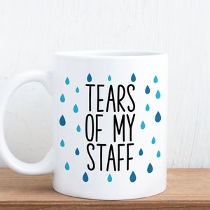 May include: White ceramic coffee mug with a black and blue design. The mug has a blue raindrop pattern and the text "Tears of my staff".