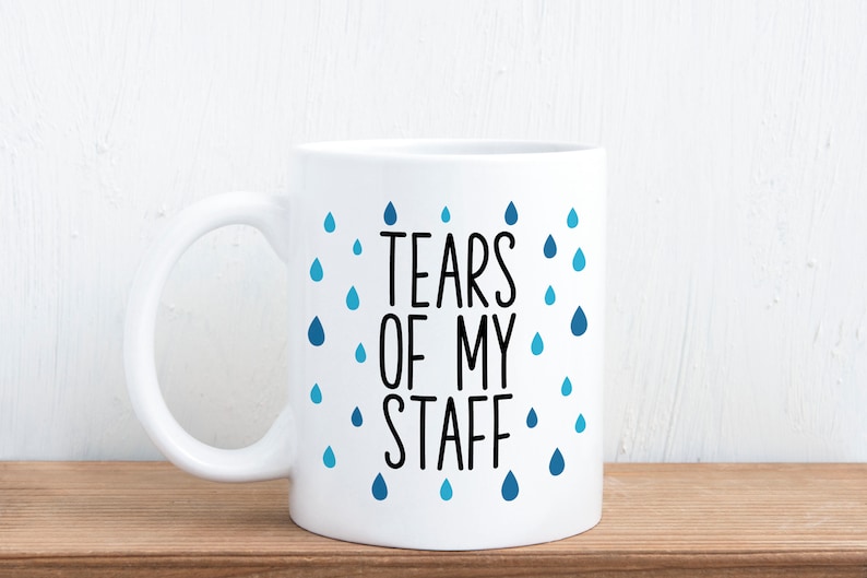 May include: White ceramic coffee mug with a black and blue design. The mug has a blue raindrop pattern and the text "Tears of my staff".