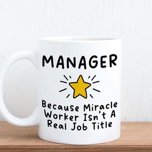May include: White ceramic coffee mug with a black outline of a star and the text "MANAGER Because Miracle Worker Isn't A Real Job Title".