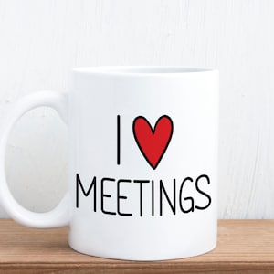 May include: White ceramic coffee mug with black text that reads "I heart meetings". A red heart is between the "I" and the "meetings".