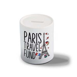 May include: White ceramic money box featuring a black and white graphic of the Eiffel Tower and the text "Paris Travel Fund". The graphic also includes a red, white and blue French flag, a croissant, and pink hearts.