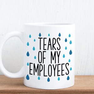 May include: White ceramic coffee mug with a black and blue design. The mug has a black text that reads "Tears of my employees" with blue raindrops surrounding the text.