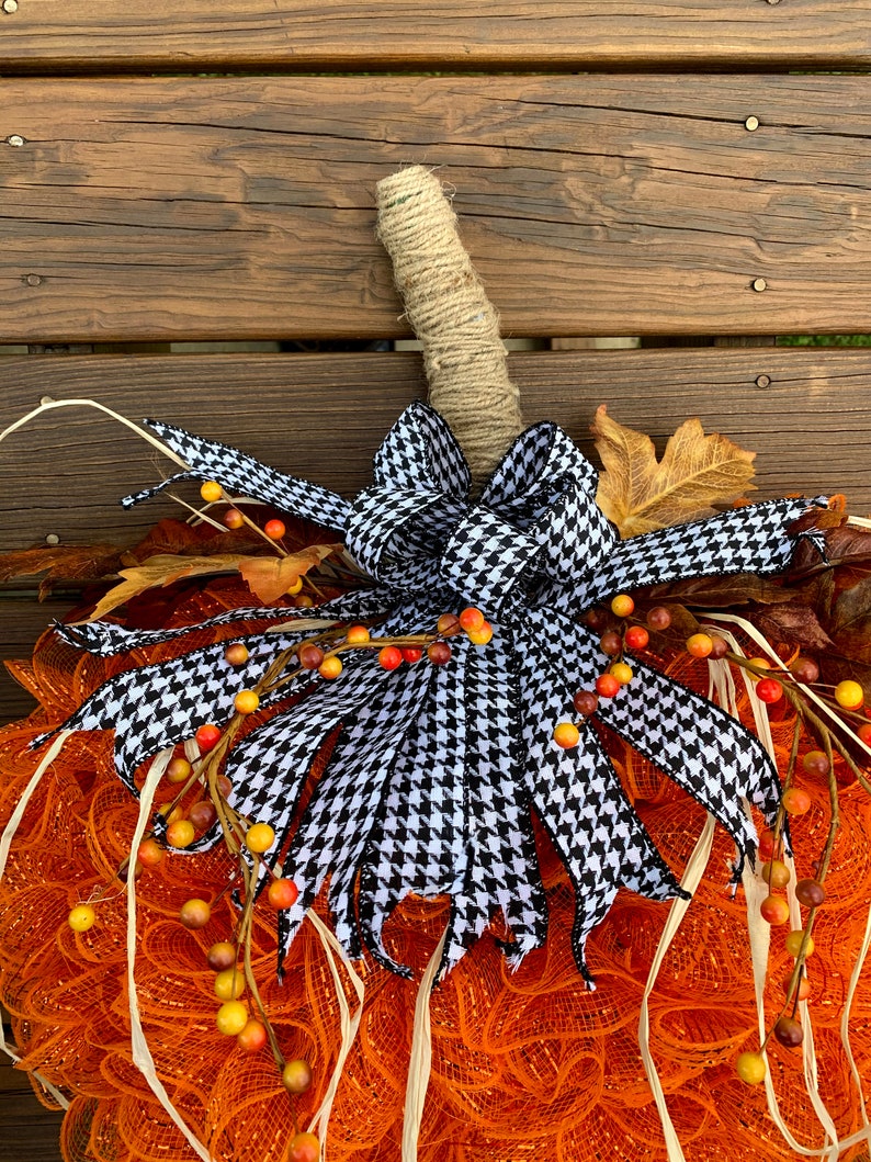 K&ouml;nnte beinhalten: Orangefarbener und wei&szlig;er Mesh-K&uuml;rbis-Adventskranz mit einer schwarzen und wei&szlig;en Hahnentritt-Schleife und Herbstlaub-Akzenten.