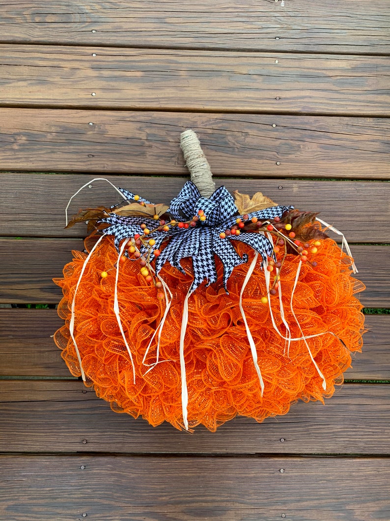K&ouml;nnte beinhalten: Orangefarbener und wei&szlig;er Mesh-K&uuml;rbis-Adventskranz mit einer schwarz-wei&szlig;en Karobinde und Herbstbeeren.
