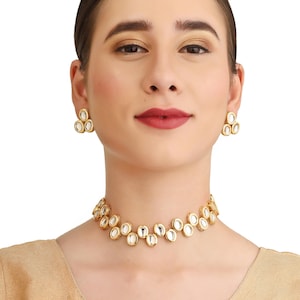 Könnte beinhalten: Goldfarbenes Halsketten- und Ohrring-Set. Der Schmuck besteht aus einer Reihe von oval geformten, verspiegelten Akzenten in einem Goldrahmen. Die Ohrringe haben eine Anordnung aus drei verspiegelten Ovalen. Die Halskette liegt am Hals.