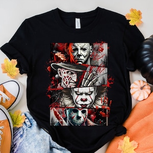 May include: Black t-shirt with a graphic of four horror movie characters: Michael Myers, Freddy Krueger, Pennywise the Dancing Clown, and Jason Voorhees. The characters are arranged in a collage style with blood splatters and other horror-themed imagery.